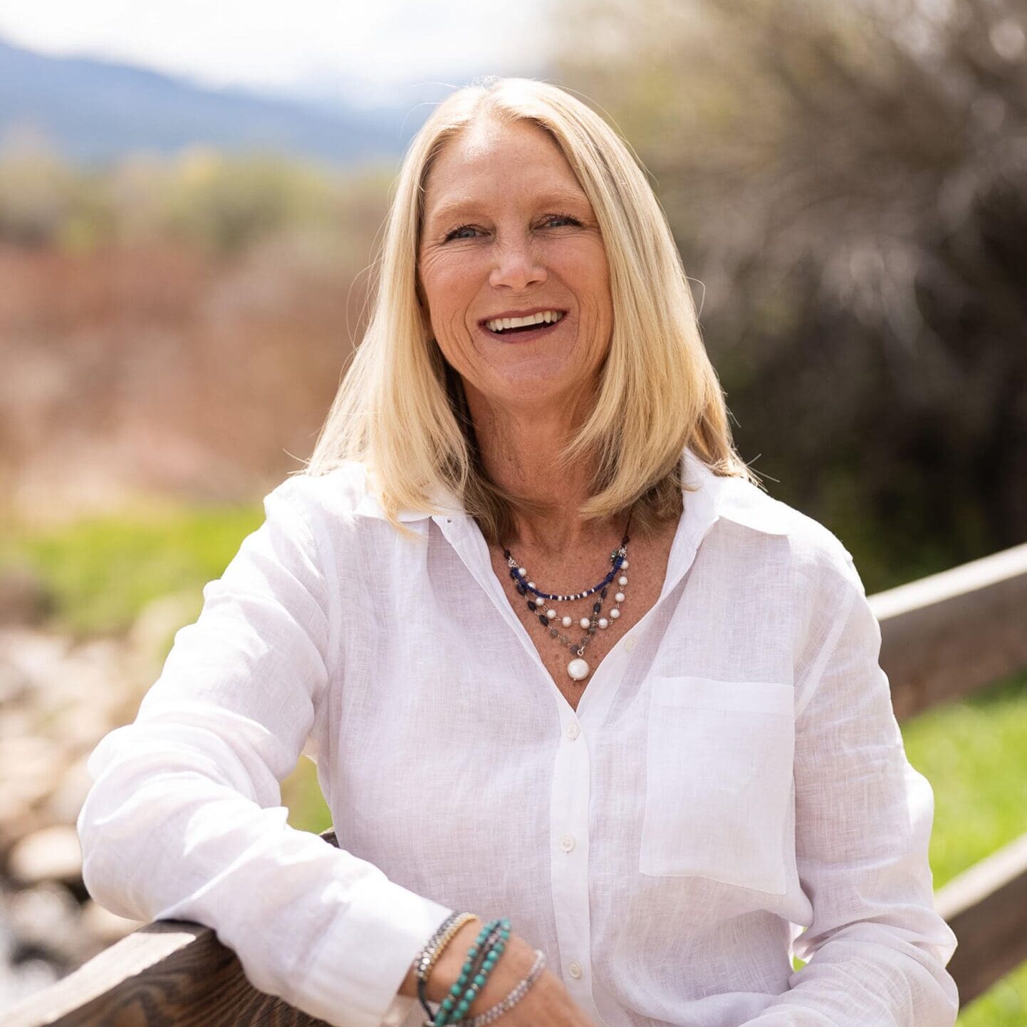 A woman in white shirt sitting on wooden rail.